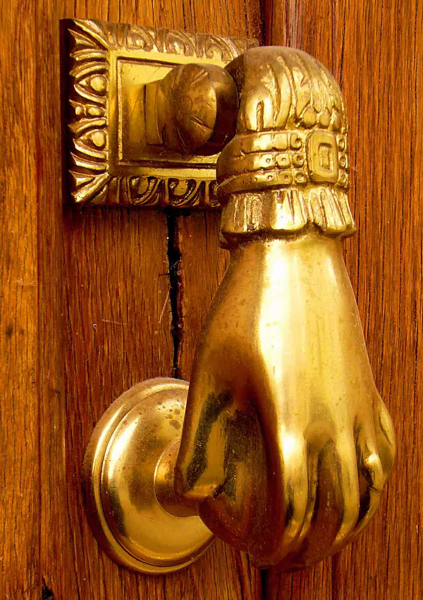 Aldaba de bronce con forma de mano sobre una puerta de madera