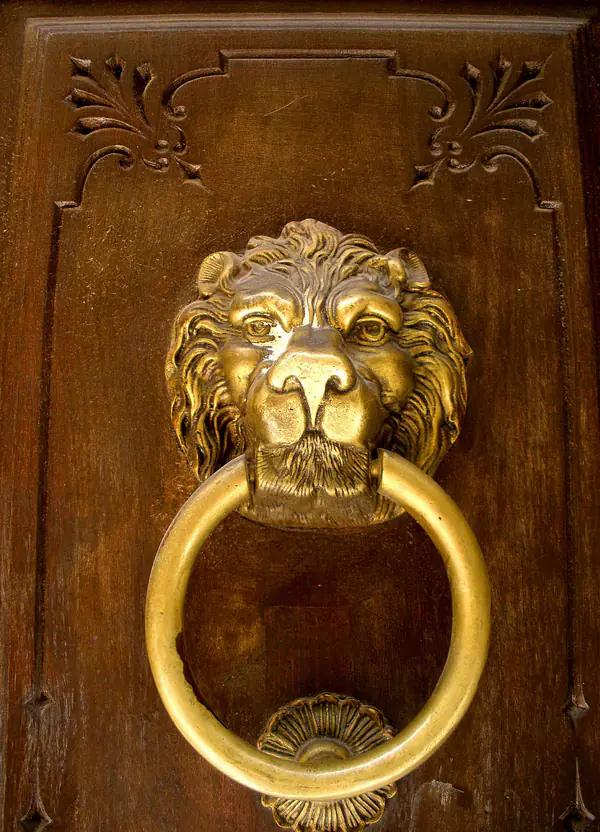 Aldaba dorada con cabeza de león en una puerta de madera