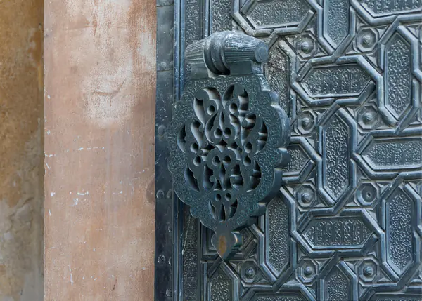 Aldaba de bronce labrado en una puerta con relieves geométricos